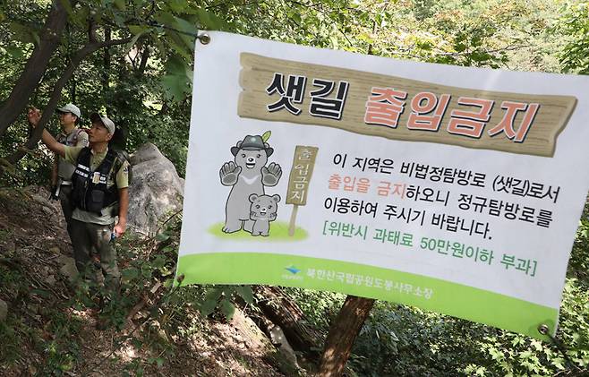 국립공원공단 직원들이 비법정 탐방로인 샛길 출입을 금지한다는 현수막 옆에서 등산객들의 출입 흔적을 살피고 있다. 국립공원에서 법정 탐방로가 아닌 샛길로 들어갔다가 적발되면 1차 20만 원, 2차 30만 원, 3차 이상 50만 원의 과태료를 내야 한다. 국립공원공단 제공