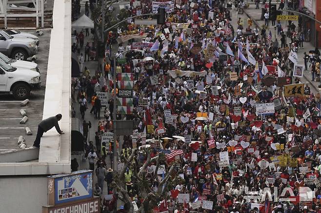 [로스앤젤레스=AP/뉴시스] 1일(현지 시간) 미 캘리포니아주 로스앤젤레스에서 노동절 시위가 열린 가운데 한 건물 꼭대기에서 한 남성이 시위대의 행진 모습을 지켜보고 있다. 2025.05.02.