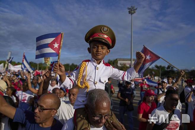 [아바나=AP/뉴시스] 1일(현지 시간) 쿠바 아바나 혁명 광장에서 열린 연례 노동절 퍼레이드 중 군복을 입은 소년이 할아버지 어깨 위에 올라타 행진하고 있다. 2025.05.02.