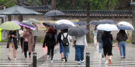 People walk with umbrellas at a crosswalk in front of Seoul City Hall in Jung District, central Seoul, on May 1. [NEWS1]