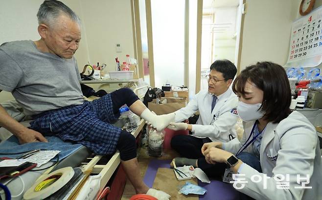 지난달 3일 광주 서구 김영준 씨(왼쪽) 자택에 서해현 시니어통합의원 원장(가운데)과 김하진 간호사가 방문해 당뇨 합병증으로 괴사된 김 씨의 발을 소독하고 있다. 장기요양 4등급인 김 씨는 광주 서구의 통합돌봄 시범사업 대상자로 선정된 뒤 매달 집에서 의사와 간호사의 진료와 더불어 생활 관리를 받고 있다. 광주=박영철 기자 skyblue@donga.com