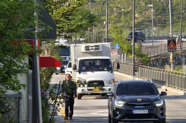 ▲ 원주 호저면 주산2리 학마을 앞 도로가 매일 출퇴근 시간대 차량들로 혼잡을 겪고 있다. 6일 마을 주민이 차량 접촉 사고 등 위험을 감수하며 비좁은 도로변을 걷고 있다.