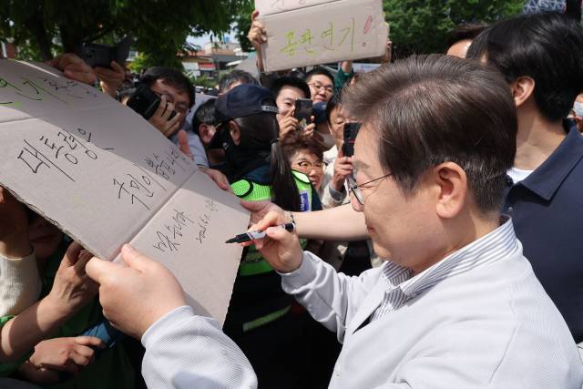 ▲더불어민주당 이재명 대선 후보가 '골목골목 경청투어:국토종주편'에 나선 7일 전북 전주시 풍남문 앞 광장에서 지지자들에게 인사를 하던 도중 한 지지자가 든 '공판 연기 환영, 대통령은 국민이 뽑습니다'라는 팻말에 사인을 하고 있다. 이날 서울고등법원은 오는 15일 예정됐던 이 후보의 공직선거법 위반 혐의 사건 파기환송심 첫 공판을 오는 6월 18일로 연기했다. ⓒ연합뉴스