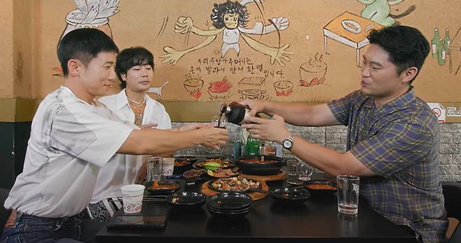 Rapper Choiza pours a glass of his bokbunja wine, Boonza, for fellow celebrities on his YouTube channel. [SCREEN CAPTURE]