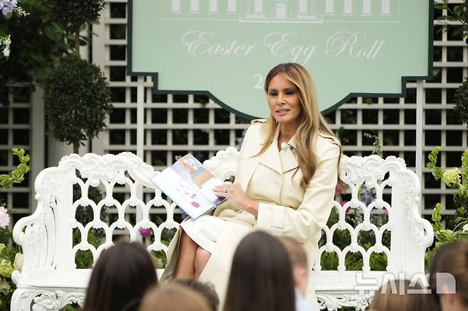 [워싱턴=AP/뉴시스] 도널드 트럼프 미국 대통령의 부인 멜라니아 여사가 21일(현지 시간) 백악관 사우스론에서 열린 연례 '백악관 부활절 달걀 굴리기' 행사에 참여한 어린이들에게 동화를 읽어주고 있다. 2025.04.22.