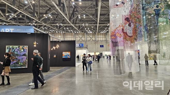 ‘아트부산 2025’ 전경. 전시장 입구에 내려진 방정아 작가의 대형 걸개형 천 작품 ‘올리버 스토의 수영’(2024, 630×320㎝ 왼쪽), ‘얼씨구 절씨구’(2024, 623×308㎝) 사이로 관람객들이 이동하고 있다. 맥화랑에서 ‘경계는 흐르고 있었고 빛은 거짓어었어’라는 타이틀로 꾸린 특별전이다(사진=오현주 문화전문기자).