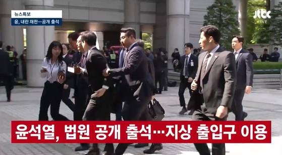 내란 우두머리 혐의로 재판을 받는 윤석열 전 대통령이 12일 법원에 공개 출석하는 과정에서 경호원이 질문하는 취재진의 팔을 잡아끌어 제지하고 있다. 〈사진=JTBC 방송화면 캡처〉