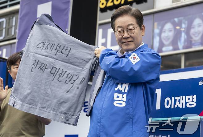 더불어민주당 이재명 대통령 후보가 14일 오후 경남 창원시 성산구 상남분수 광장에서 한 지지자가 건넨 '이제부터 진짜 대한민국!'이라는 선거 문구가 적힌 옷을 바라보고 있다. (공동취재) 2025.5.14/뉴스1 ⓒ News1 안은나 기자