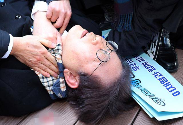 지난해 1월 2일 이재명 당시 더불어민주당 대표가 부산 가덕도 신공항 부지를 둘러본 뒤 취재진과 질의응답을 하며 차량으로 이동하는 과정에서 괴한으로부터 흉기 피습을 당해 쓰러져 있다. 부산=연합뉴스