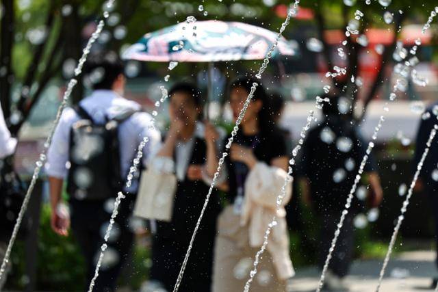 서울 한낮 기온이 26도까지 오르면서 초여름 날씨를 보인 14일 서울 종로구 광화문 광장에서 양산을 쓰고 겉옷을 손에 든 시민이 분수 앞을 지나고 있다. 연합뉴스