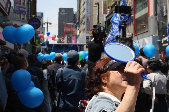 이재명 더불어민주당 대선 후보가 14일 부산 부산진구 서면거리에서 유권자들에게 지지를 호소하고 있는 가운데 지지자가 저격수의 시야를 방해하기 위해 거울로 주변 건물을 향해 빛을 반사시키고 있다. 부산=오승현 기자 2025.05.14