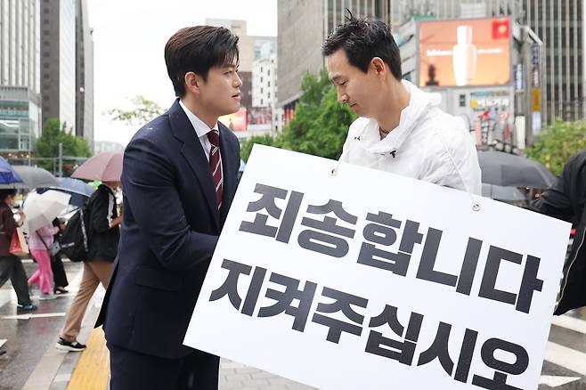 김용태(왼쪽) 국민의힘 비상대책위원장이 16일 서울 광화문광장에서 국민의힘 지지를 호소하는 내용의 팻말을 들고 있는 김기흥 전 대통령실 부대변인을 격려하고 있다./뉴스1