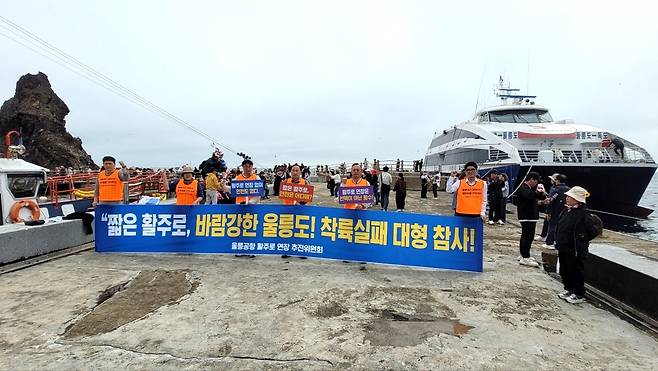 17일 독도 선착장에서 ‘울릉공항 활주로 연장 추진위원회’가 울릉공항 활주로 연장을 촉구하며 현수막을 들고 구호를 외치고 있다.[울릉공항 활주로 연장 추진위원회 제공]