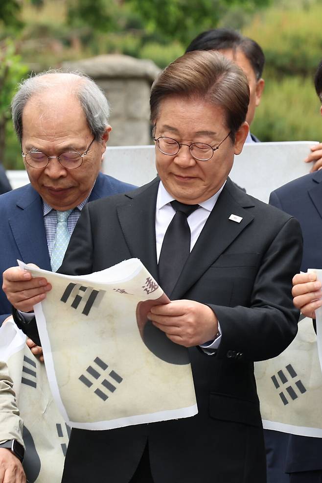 이재명 더불어민주당 대선 후보가 19일 서울 용산구 백범김구 묘역을 참배하기에 앞서 태극기를 살펴보고 있다. ⓒ공동취재