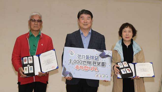 조원용 경기관광공사 사장(가운데)이 '경기둘레길' 999, 1000번째 완보자인 성판득씨(왼쪽)와 이은영씨(오른쪽) 부부에게 완보증과 기념품을 전달하며 기념촬영을 하고 있다./사진제공=경기관광공사