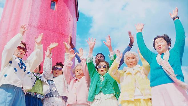 “파란 하늘, 분홍 등대, 그리고 칠곡할매들” 통영의 분홍 등대 앞에서 두 손을 번쩍 들고 환호하는 수니와칠공주. 영상제작에 동참한 아프리카 출신의 외국인 아티스트 ‘온유 와의 호흡도 자연스럽다./칠곡군 제공