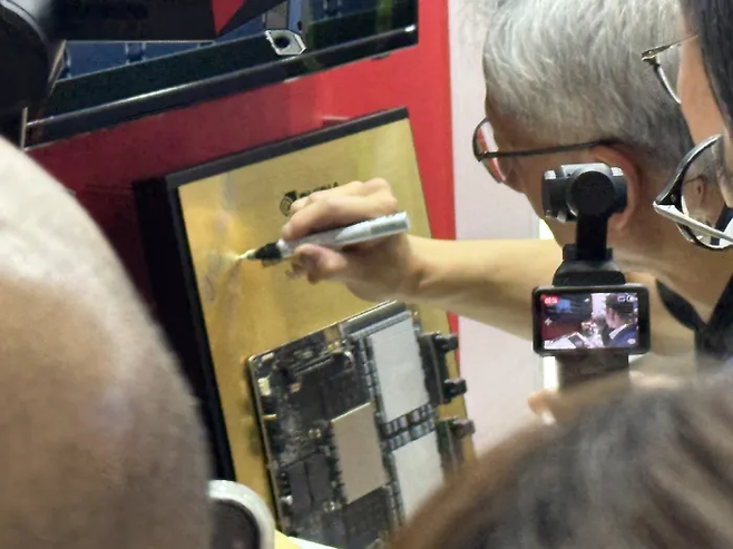 젠슨 황 엔비디아 CEO가 지난 20일 대만 타이베이 난강 전시관에서 개최된 ‘컴퓨텍스 2025’에서 SK하이닉스 부스를 찾아 전시된 HBM에 사인하고 있다. 연합뉴스