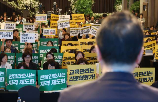 박민수 보건복지부 2차관이 21일 서울 용산구 피스앤파크컨벤션에서 열린 간호법 제정에 따른 진료지원업무 제도화 방안 공청회에서 인사말을 하는 동안 대한간호협회 회원들과 공공운수노조 의료연대본부 조합원들이 항의 피켓을 들고 있다. 뉴스1