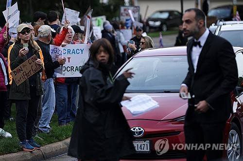 트럼프 밈코인 행사에 항의하는 시위대 (스털링<미 버지니아주> AFP=연합뉴스) 2025년 5월 22일 미국 버지니아주 스털링에 있는 트럼프 내셔널 골프 클럽에서 열린 비공개 만찬 행사에 항의하는 시위가 열리고 있는 와중에, 만찬에 초대된 한 초청객이 도착하고 있다. (Getty Images via AFP) 2025.5.24.