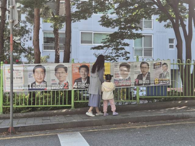 25일 울산시 남구 신정동 한 아파트 단지 앞 인도에서 한 모녀가 손을 잡고 걷다가 선거벽보를 보며 이야기를 나누고 있다.
