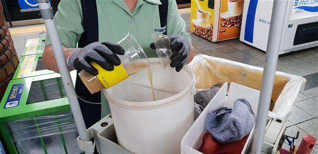 분리수거함 위에 버려져 있는 일회용 컵들(왼쪽사진). 환경미화원이 음료수컵에 남은 액체를 분리하고 있는 모습.[헤럴드DB]