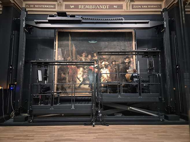 유리 창살 속에 갇혀서 복원 중인 렘브란트의 [야경]. 거의 복원을 마친 그림의 왼쪽과 오른쪽 끝 부분은 바니시가 제거되지 않아 흐릿하게 보인다. ©김슬기