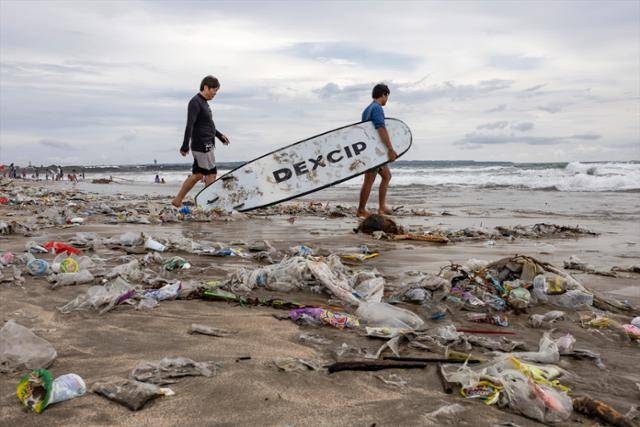 지난해 12월 인도네시아 발리섬 꾸따 해변에서 서퍼들이 플라스틱 쓰레기가 가득한 모래사장을 지나고 있다. 발리=EPA 연합뉴스 자료사진