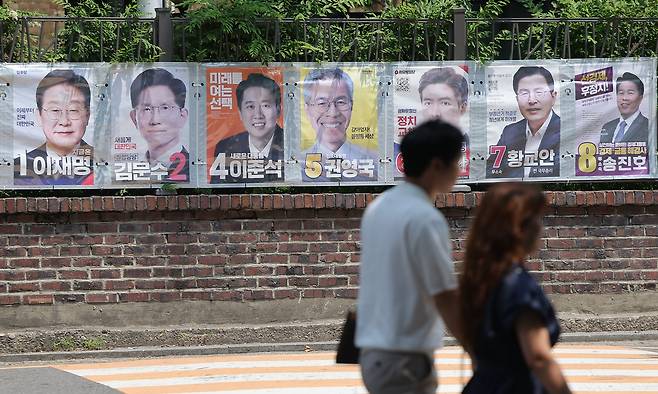 Citizens pass by a display of presidential campaign posters in central Seoul, on Sunday. From left: Lee Jae-myung of the liberal Democratic Party; Kim Moon-soo of the major conservative People Power Party; Lee Jun-seok of the minor conservative New Reform Party; Kwon Young-guk of the Democratic Labor Party; Koo Ju-hwa of the Liberty Unification Party; Hwang Kyo-ahn, an independent; and Song Jin-ho, an independent. (Yonhap)