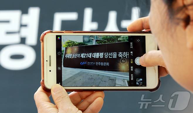 4일 이재명 대통령의 모교인 서울 동작구 중앙대학교에서 한 시민이 당선 축하 현수막을 스마트폰으로 촬영하고 있다. 이 대통령은 1728만7513표를 얻어 득표율 49.42%로 당선됐다. 2025.6.4/뉴스1 ⓒ News1 김진환 기자