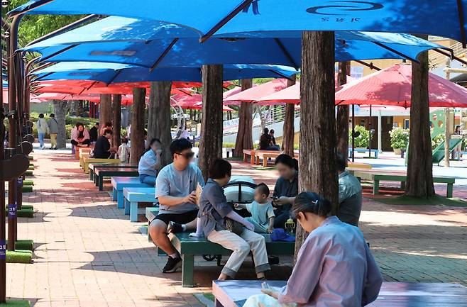 4일 부산 기장군 정관 윗골공원 야외 물놀이장 주변에 대형 그늘막과 평상이 설치돼 방문객들이 앉아 더위를 식히고 있다. [사진 출처 = 연합뉴스]