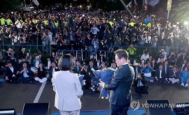 국민개표방송 행사장 찾은 이재명 후보 내외 (서울=연합뉴스) 김주성 기자 = 제21대 대통령 당선이 확실시되는 더불어민주당 이재명 대선 후보와 부인 김혜경 여사가 4일 서울 여의도 국회 인근에서 당 주최로 열린 국민개표방송 행사에 참석해 꽃다발을 받은 뒤 시민들과 소통하고 있다. 2025.6.4 [공동취재] utzza@yna.co.kr