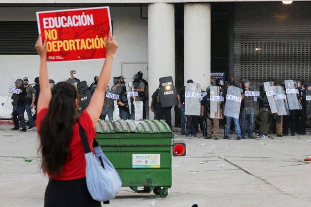6일 미국 캘리포니아주 로스앤젤레스(LA) 시내에서 이민세관단속국(ICE)에 의한 불법 이민자 단속이 진행되자 LA 연방청사 앞에서 한 시위참가자가 경찰 앞에서 플래카드를 들고 있다. LA=로이터 연합뉴스