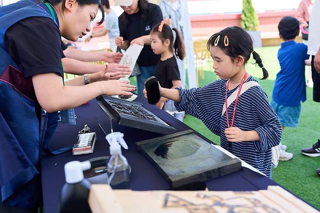 '제3회 독립출판 북페어 전주책쾌'를 찾은 한 여자아이가 전문가 도움을 받아 목판 인쇄 체험 '책쾌는 내 손 안에'를 하고 있다. 사진 전주시