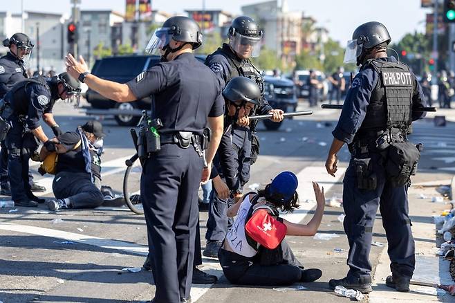 2025년 6월 8일, 캘리포니아 로스앤젤레스에서 연방 이민 단속 이후 벌어진 시위 도중, 연방 정부 청사를 둘러싼 거리에서 시위대와 경찰이 충돌하는 가운데 한 여성이 체포되고 있다. 이날 로스앤젤레스에서는 시위대가 차량에 불을 지르고 보안군과 충돌했으며, 경찰은 도널드 트럼프 대통령이 미국 제2의 도시인 로스앤젤레스 거리로 파견한 주방위군 병력에 시위대가 접근하지 못하도록 막았다. [사진 = AFP 연합뉴스]