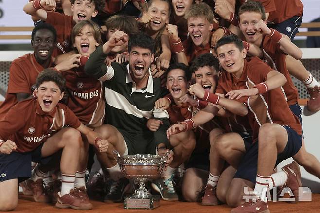 [파리=AP/뉴시스] 카를로스 알카라스(2위·스페인)가 8일(현지 시간) 프랑스 파리 롤랑가로스에서 열린 프랑스오픈 남자 단식 정상에 올라 트로피를 들고 볼키즈와 함께 기념 촬영하고 있다. 알카라스는 결승전에서 얀니크 신네르(1위·이탈리아)와 5시간 29분 대접전 끝에 3-2(4-6 6-7 6-4 7-6 7-6) 역전승을 거두고 대회 2연패를 달성했다. 2025.06.09.