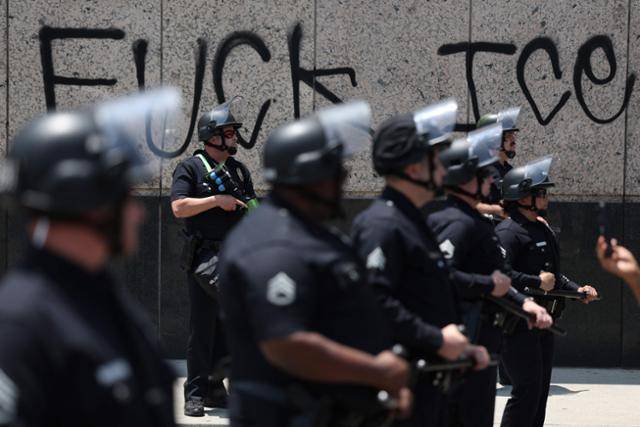 9일 로스앤젤레스 메트로폴리탄 구치소 인근에서 연방 이민국 단속에 항의하는 시위대가 모여 있는 가운데 경찰이 "Fuck ICE(이민세관단속국)"라고 쓰인 낙서 옆에 서 있다. 로스앤젤레스=AFP 연합뉴스