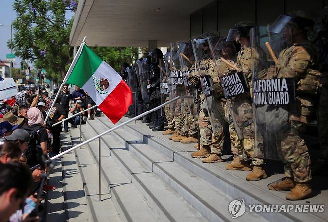 9일 LA 도심에 배치된 주방위군 앞에서 멕시코 깃발 흔드는 집회 참가자들 [로이터=연합뉴스. 재판매 및 DB 금지]