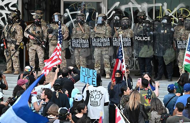 캘리포니아 주 방위군과 미국 세관·국경보호국은 10일(현지시간) 미국 로스앤젤레스(LA)에서 며칠간 미등록 이민자 반대 시위가 이어지는 가운데 연방 건물 앞에 모인 시위대를 바라보고 있다. AFP연합뉴스