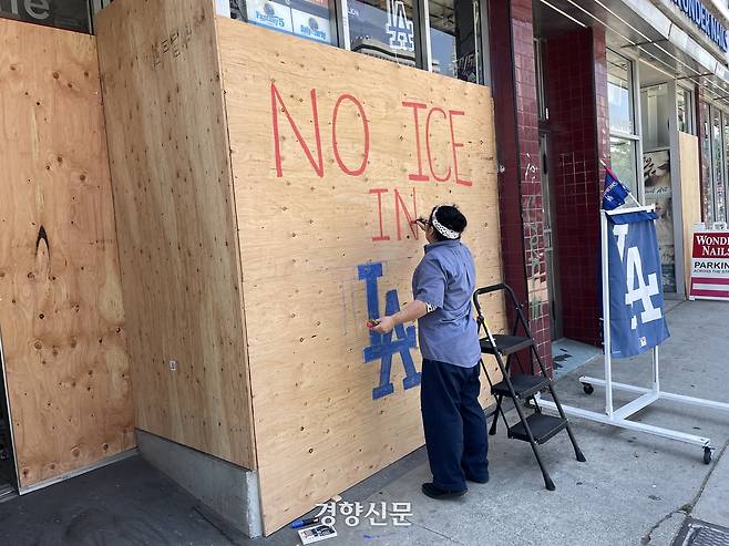 도널드 트럼프 미국 행정부의 이민 단속에 항의하는 시위가 열리는 10일(현지시간) 로스앤젤레스(LA) 도심 인근 리틀도쿄의 한 상점 직원이 약탈에 대비해 가게 문 앞에 세운 나무 판자벽 위에 ‘ICE는 LA에서 없어져야 한다’는 글씨를 적고 있다. 로스앤젤레스 | 김유진 특파원