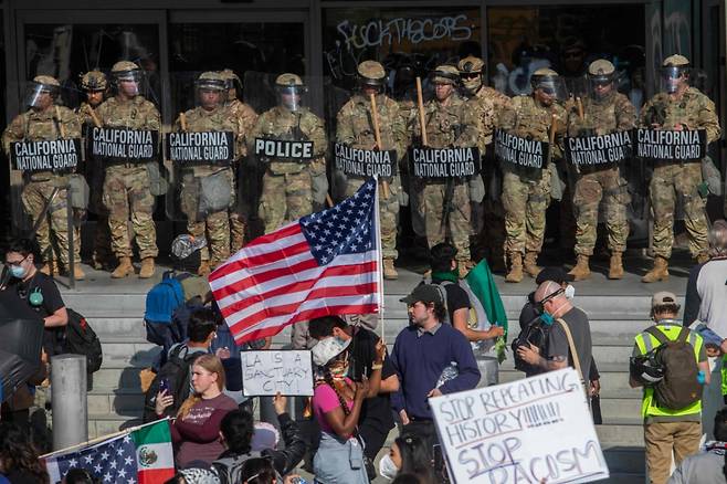 2025년 6월 9일 로스앤젤레스에서 연방 이민 작전에 반대하는 시위대가 연방 건물 밖에서 경비를 서고 있는 캘리포니아 주방위군 대원들을 향해 피켓과 깃발을 들고 있다.   /AFPBBNews=뉴스1