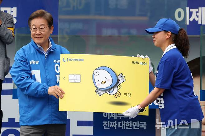[파주=뉴시스] 조성우 기자 = 이재명 대통령이 더불어민주당 대선후보 당시  경기 파주시 금릉역 중앙광장에서 열린 유세에서 선거운동원으로부터 경기지역화폐 파주페이 모형을 받고 있다. 2025.05.20. xconfind@newsis.com