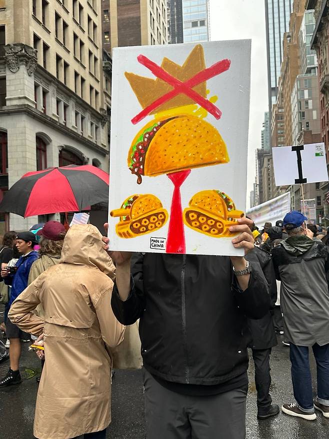 14일 뉴욕에서 열린 시위에 한 시민이 타코 그림을 들고 나왔다. 최근 도널드 트럼프 대통령의 정책을 ‘타코(트럼프는 항상 겁먹고 도망친다·Trump Always Chickens Out)’라고 비꼰 것을 나타냈다.