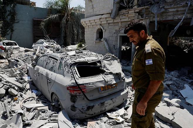 15일(현지시간) 이스라엘 북부 탐라의 주거용 건물에 이란에서 발사된 미사일이 충돌한 후 한 이스라엘 군인이 손상된 차량 근처에 서 있다. 사진=REUTERS