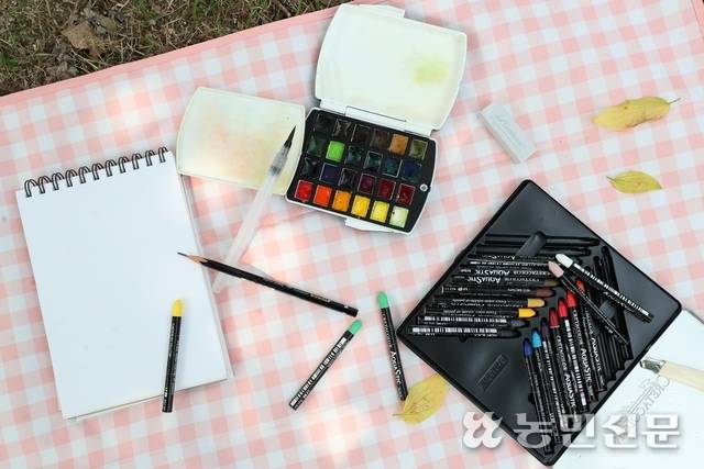 1인용 돗자리 위에 작은 스케치북과 그림 도구를 펼쳐놓은 모습.
