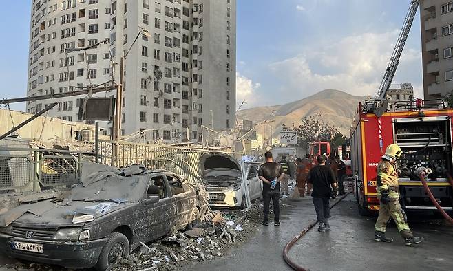 지난 13일(현지시각) 이란 테헤란 북쪽 지역에서 이스라엘 공습으로 건물과 차량이 부서진 가운데 소방 당국이 수습에 나서고 있다. EPA 연합뉴스