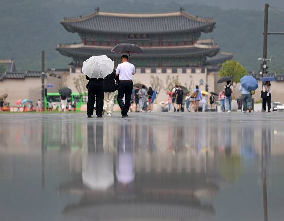 비가 내린 가운데 서울 광화문광장에 고인 빗물 위로 광화문과 우산을 쓴 시민의 모습이 비치고 있다. [사진=연합뉴스]