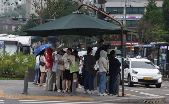 13일 오후 서울 종로구 세종대로사거리에서 시민들이 그늘막 아래에 서서 비를 피하고 있다. 뉴시