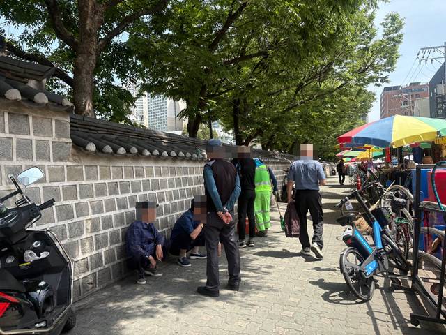 서울 한 고등학교 근처에서 사람들이 담배꽁초를 치우는 환경미화원 옆에서 담배를 피우는 모습.