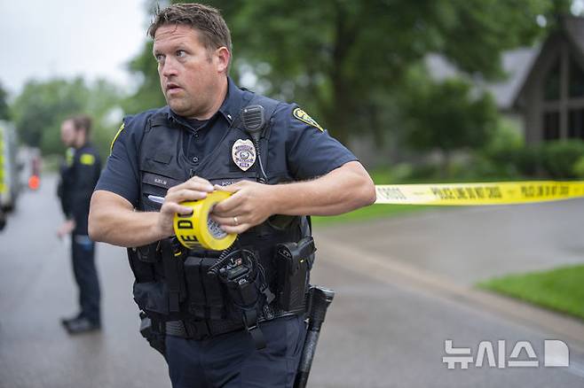 [미네소타주=AP/뉴시스] 브루클린 파크 경찰서의 한 경찰관이 14일 미네소타주 브루클린 파크에서 발생한 총격 사건 현장 인근에 경찰 경계선을 설치하고 있다. 2025.06.16.