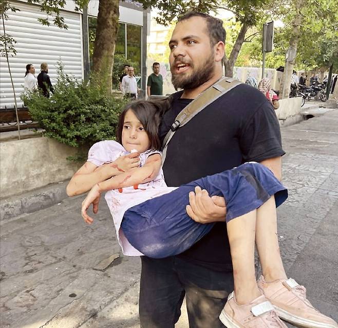 < 민간인 피해 속출 > 이스라엘과 이란 간 교전으로 사상자가 속출하고 있다.  같은 날 이란 테헤란에서 한 남성이 이스라엘 공습으로 다친 아이를 안고 대피하고 있다.  AP연합뉴스